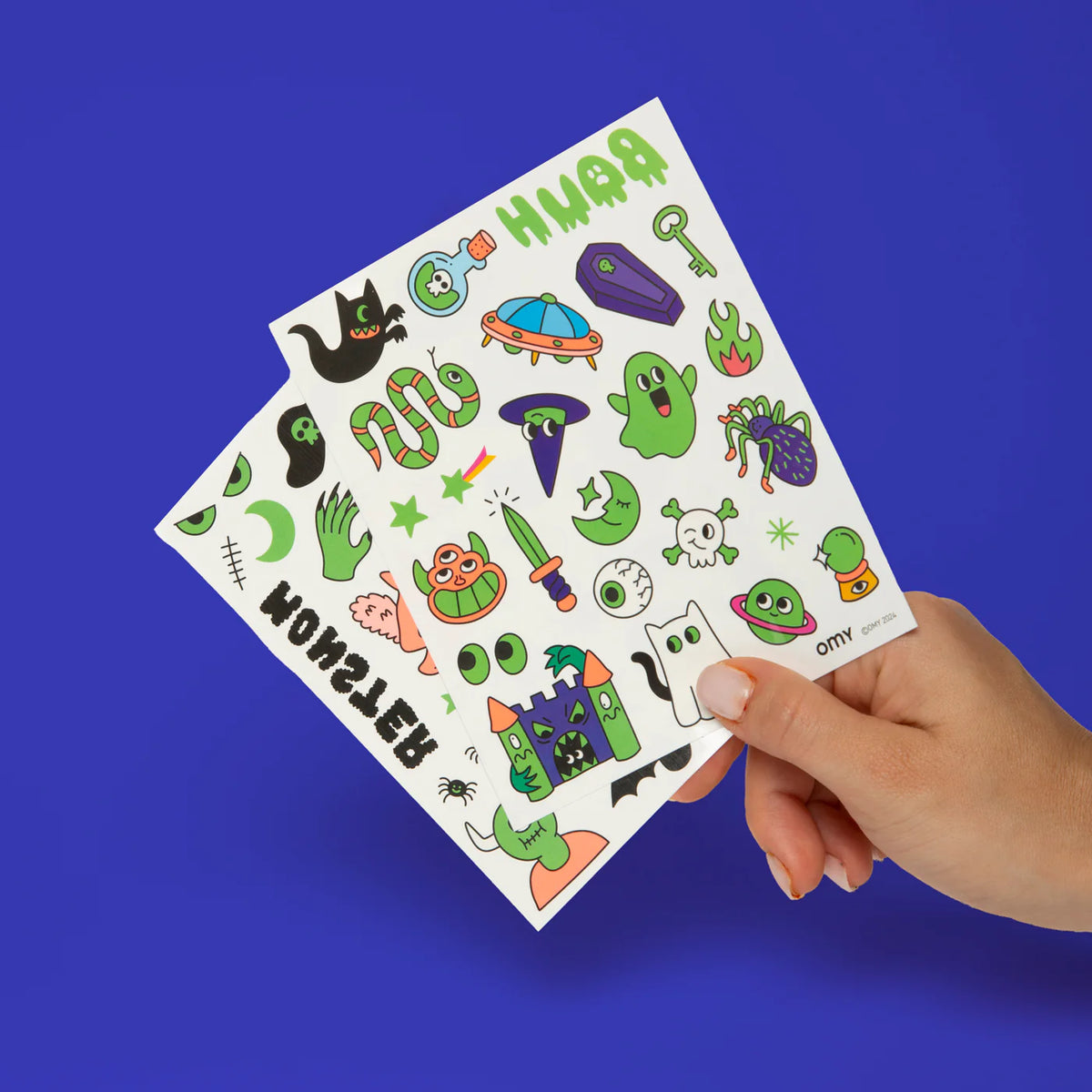 Hand holding a sheet of colorful Halloween-themed tattoos against a blue background