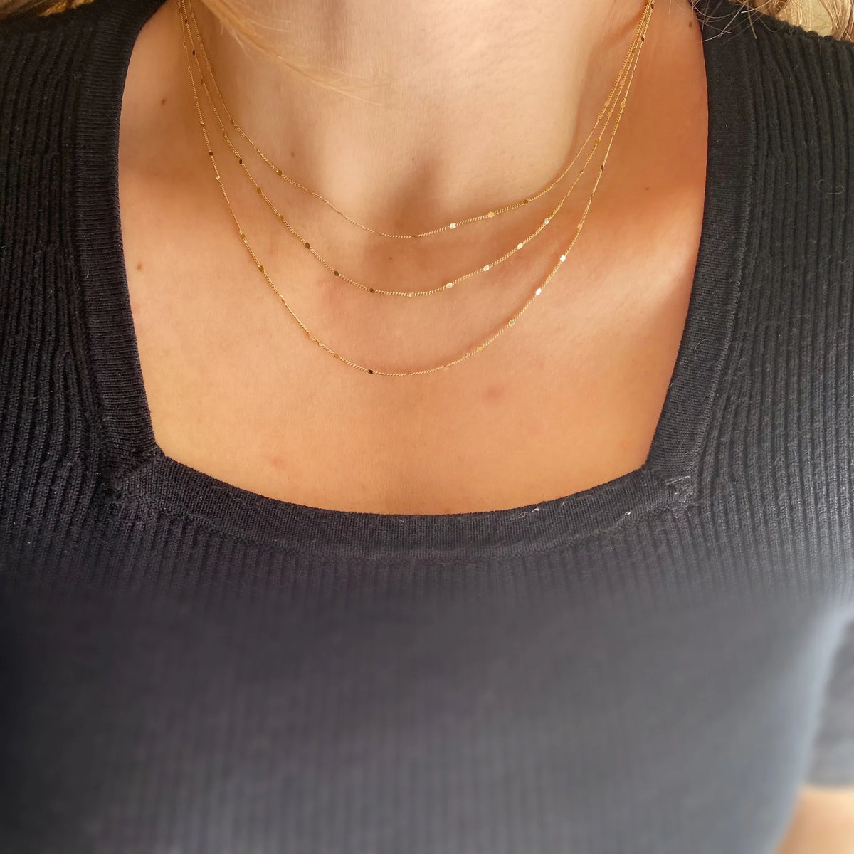 Close-up of a person wearing a black top with a gold necklace.