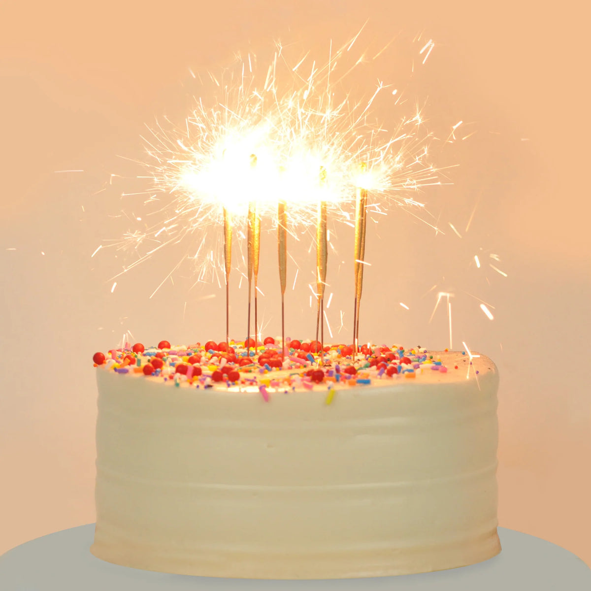 Birthday cake with lit sparklers on a light background
