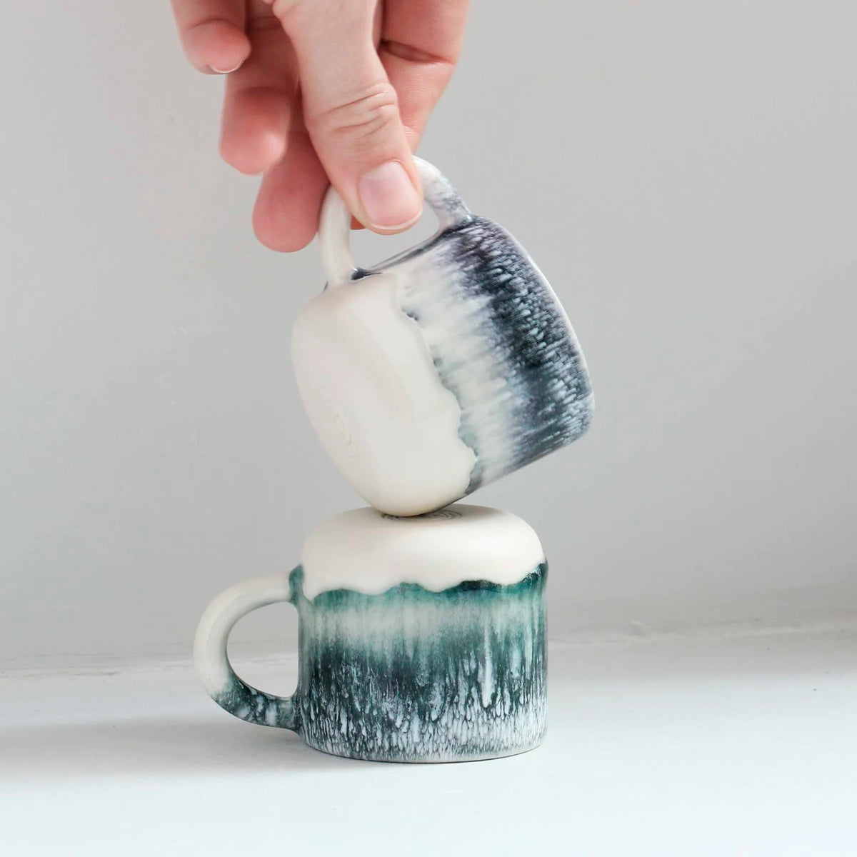 Two ceramic mugs with gradient design being stacked on a plain background
