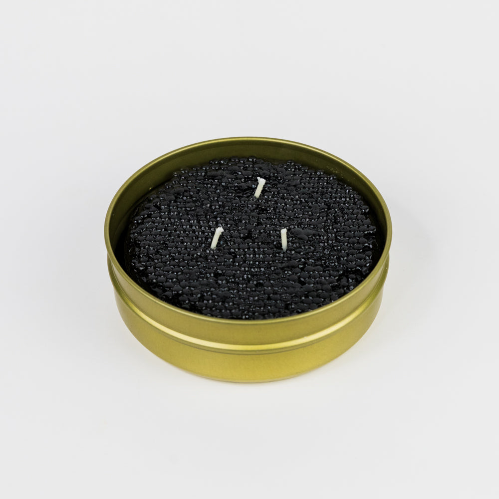 Black candle in a gold tin on a white background